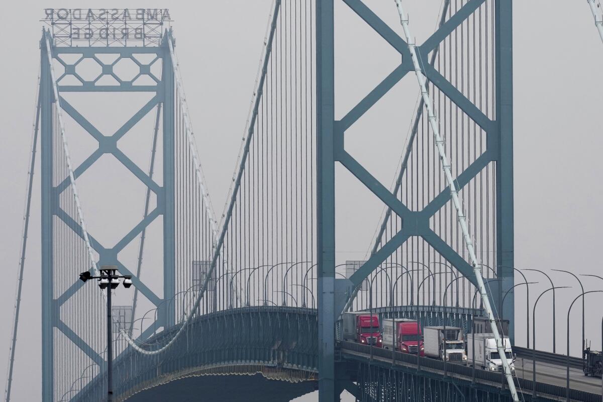 Trucks driving on a blue-gray suspension bridge.