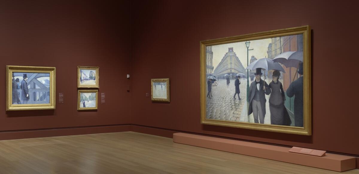 The painting "Paris Street, Rainy Day" hangs on a gallery wall with other works by Gustave Caillebotte.