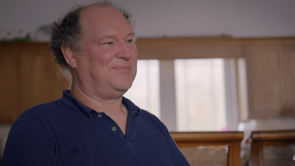 A man in a blue polo shirt sits and looks to his right.