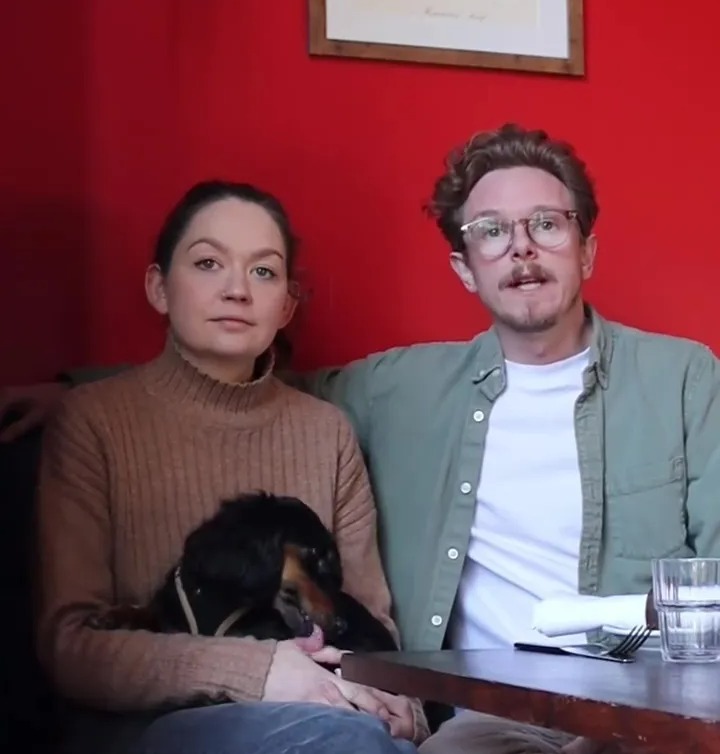 Couple and dog sitting at a table.