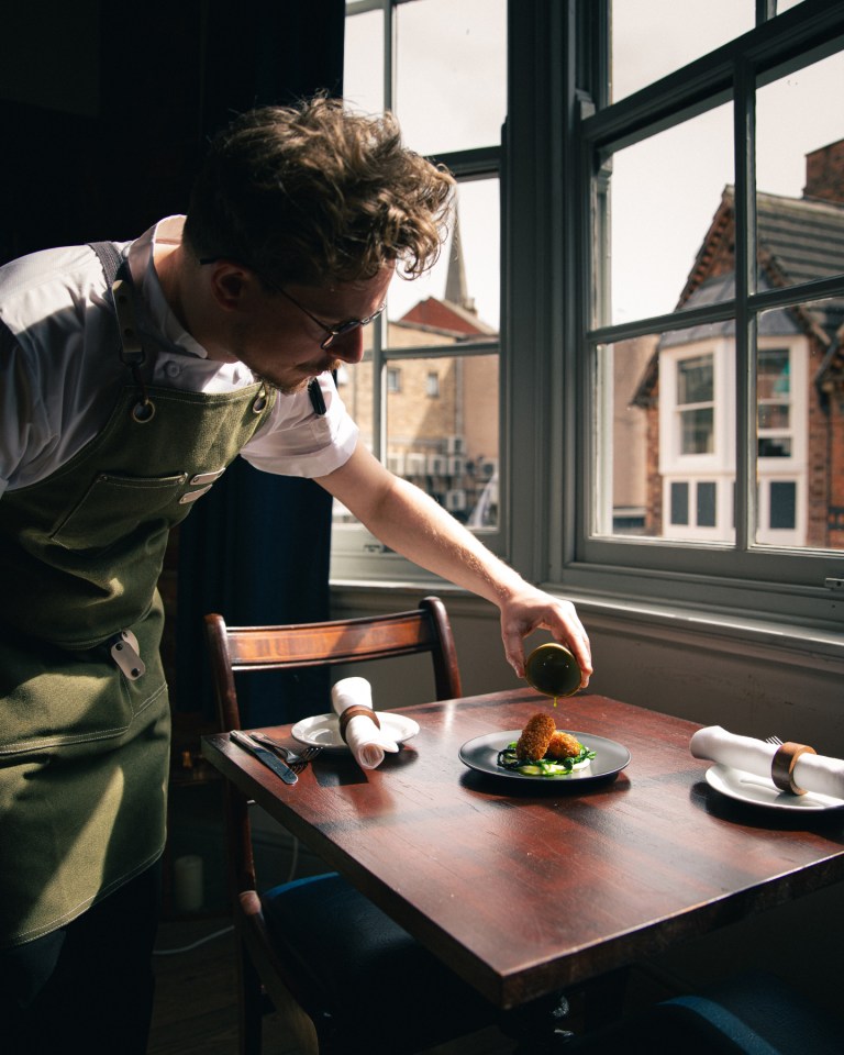 Chef plating food at a table by a window.