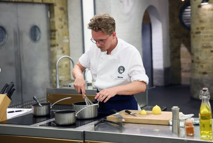 A chef in a white jacket whisks a sauce in a saucepan.