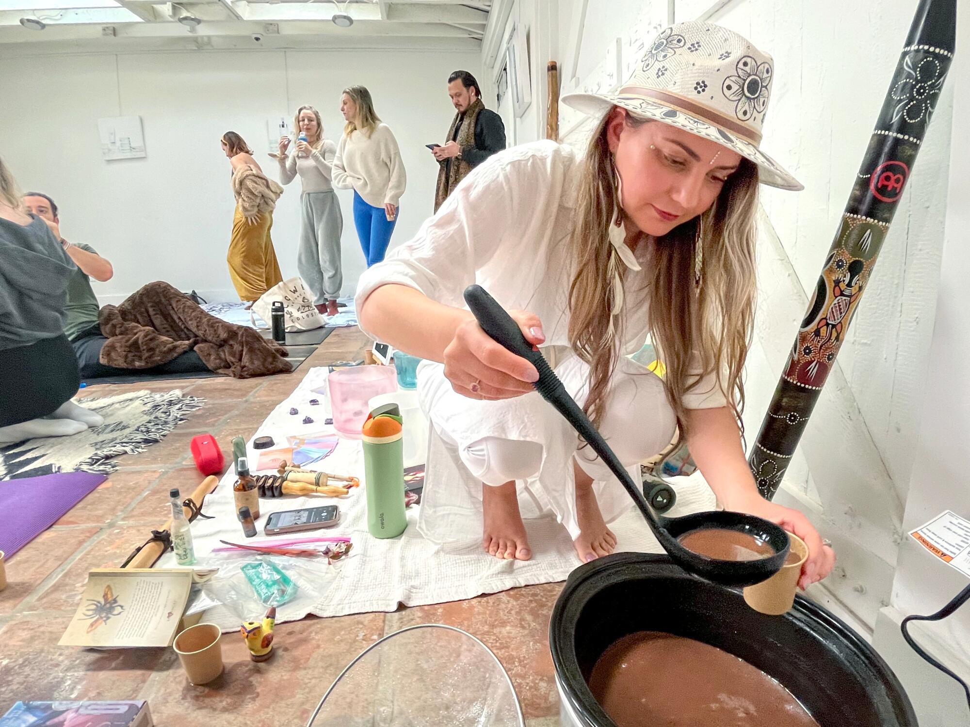 A woman in a hat ladles cacao from a pot. 