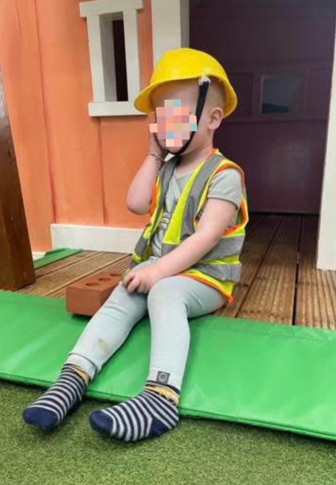 Toddler in a hard hat and safety vest playing with a toy brick.