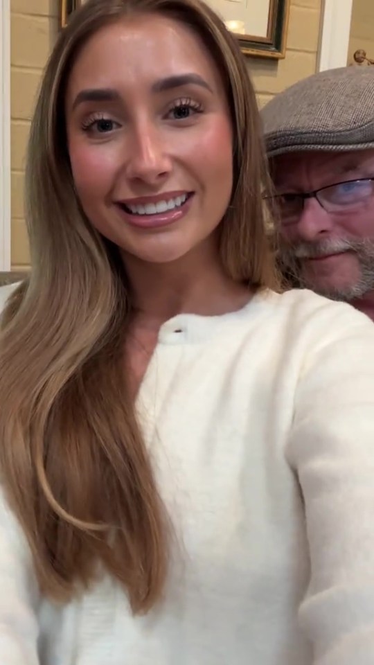 Woman in white cardigan with man behind her.