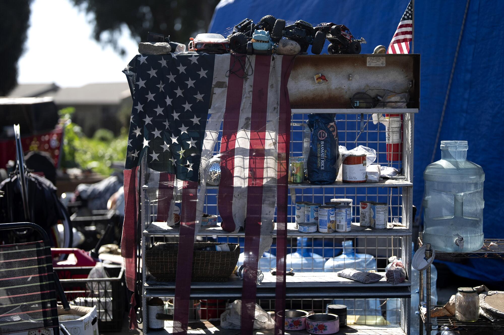 An outdoor bookcase at a homeless camp is lined with tools, cans and other supplies.