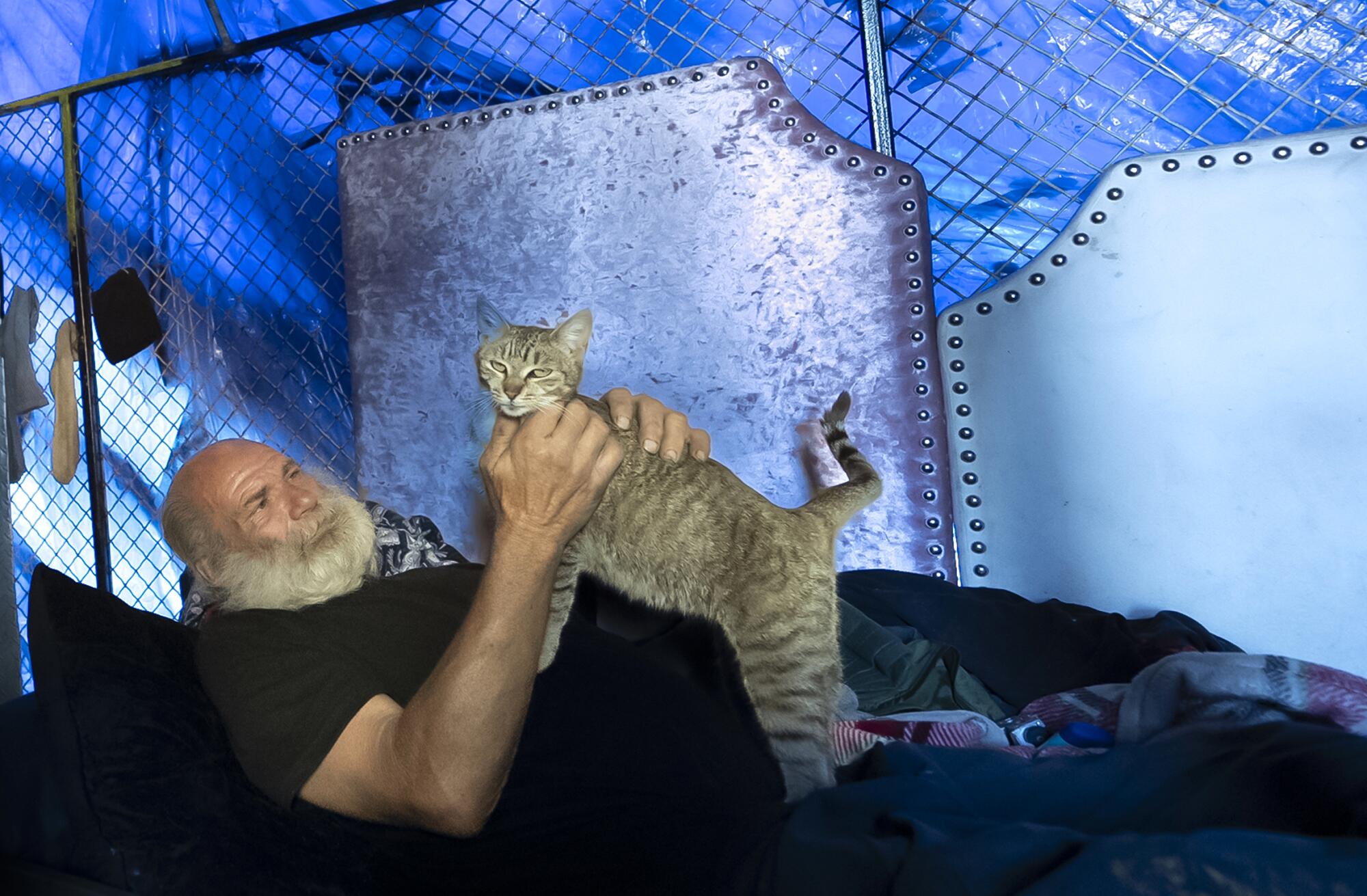 A man pets a tan cat while reclined in an expansive tent structure. 