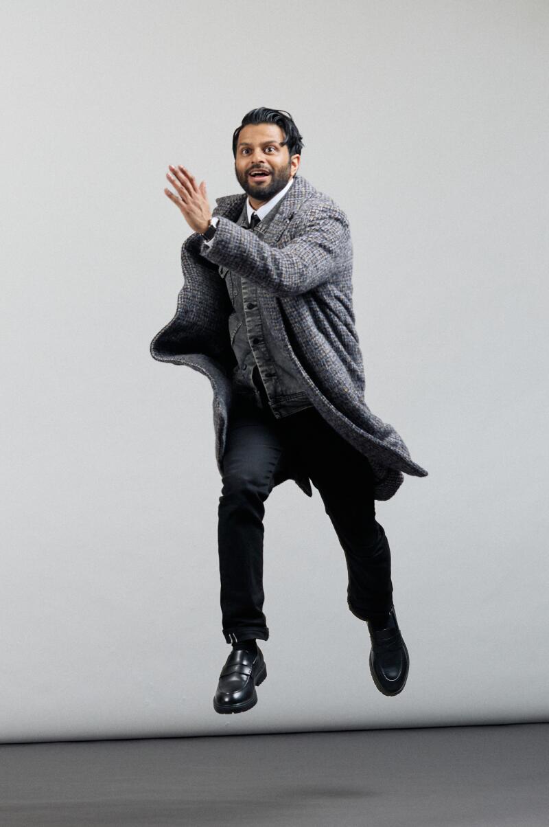 A man in a gray coat jumps in the air with an arm outstretched in front of him.