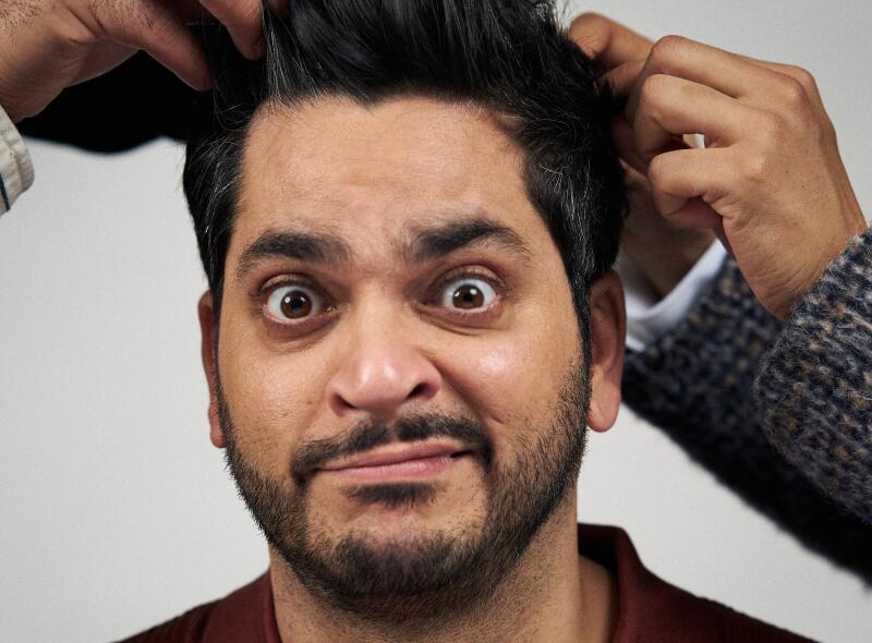 A man smirking as his hair is being pulled by two pairs of hands in the frame.