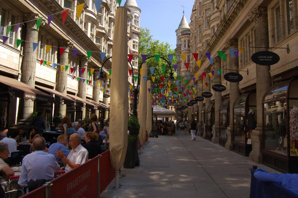 Sicilian Avenue in Holborn, London, with outdoor cafes and shops decorated with colorful flags.