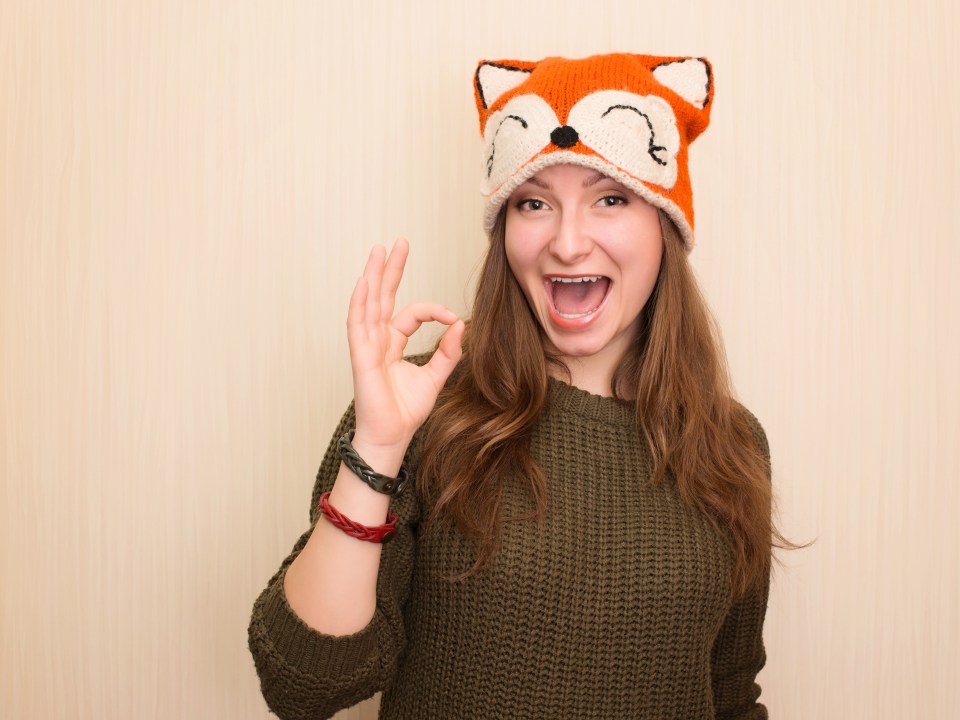 Cheerful hipster girl wearing a fox hat giving the okay gesture.