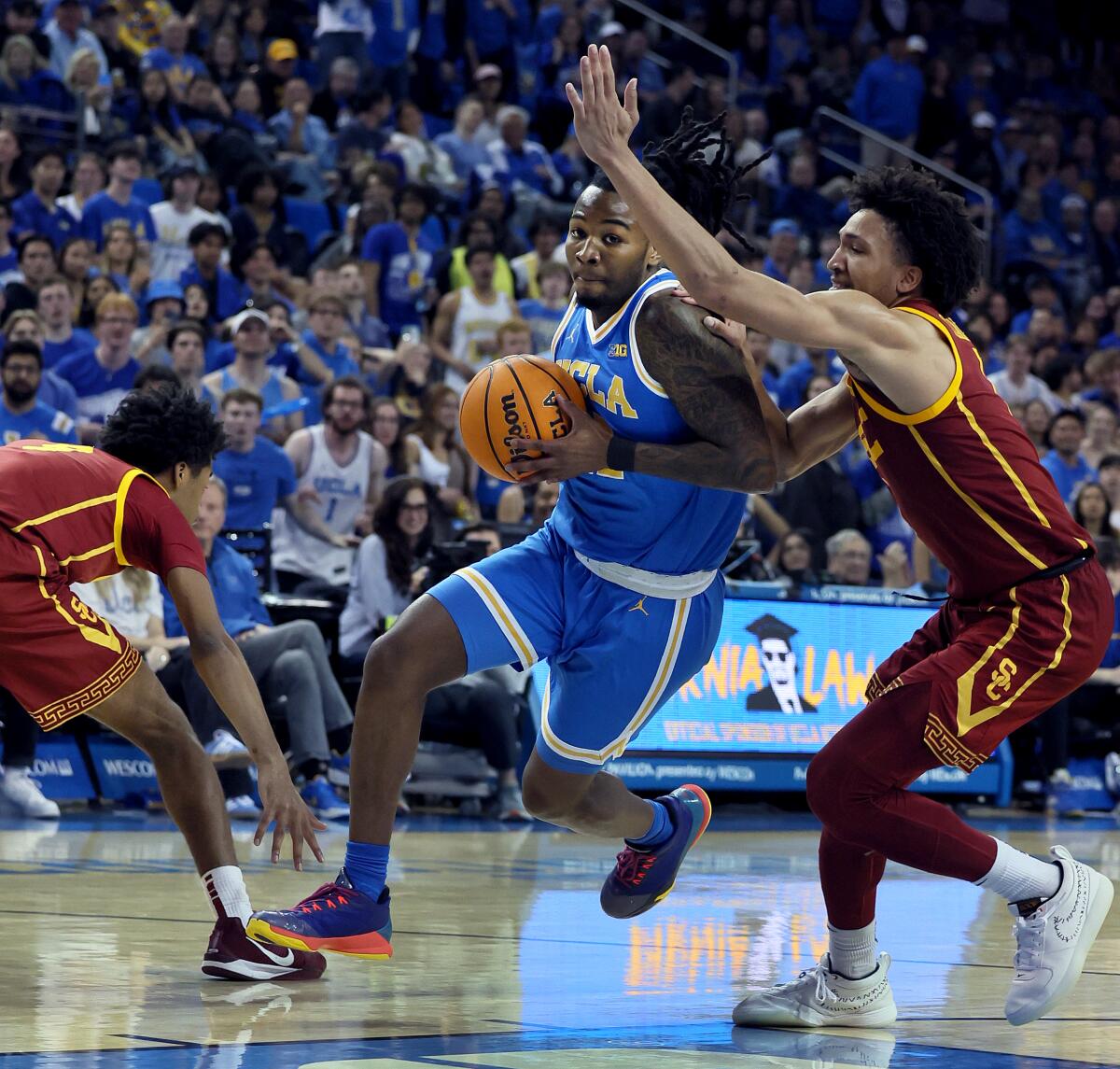 UCLA's Sebastian Mack, center, drives between USC's Jalen Shelley, left, and Desmond Claude.