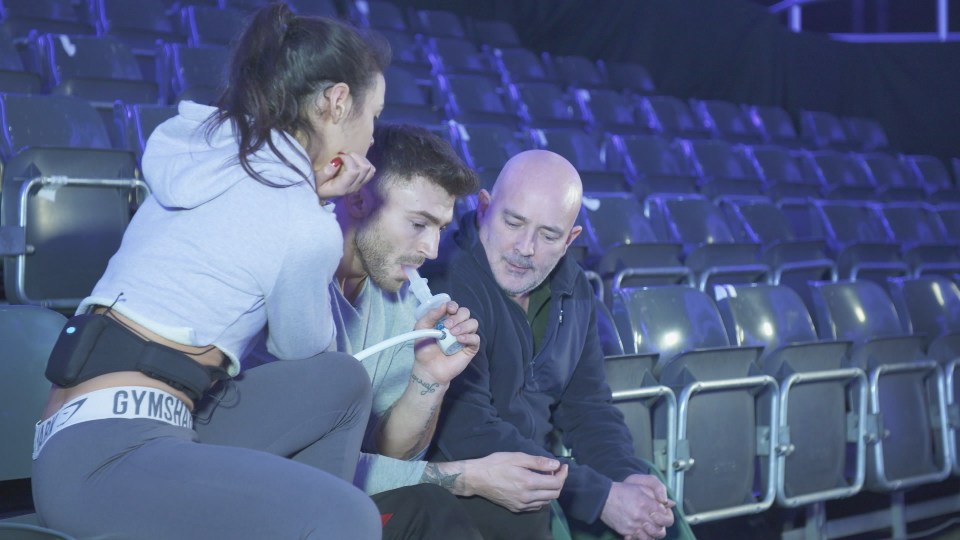 A man using an inhaler while sitting with two other people in an arena.