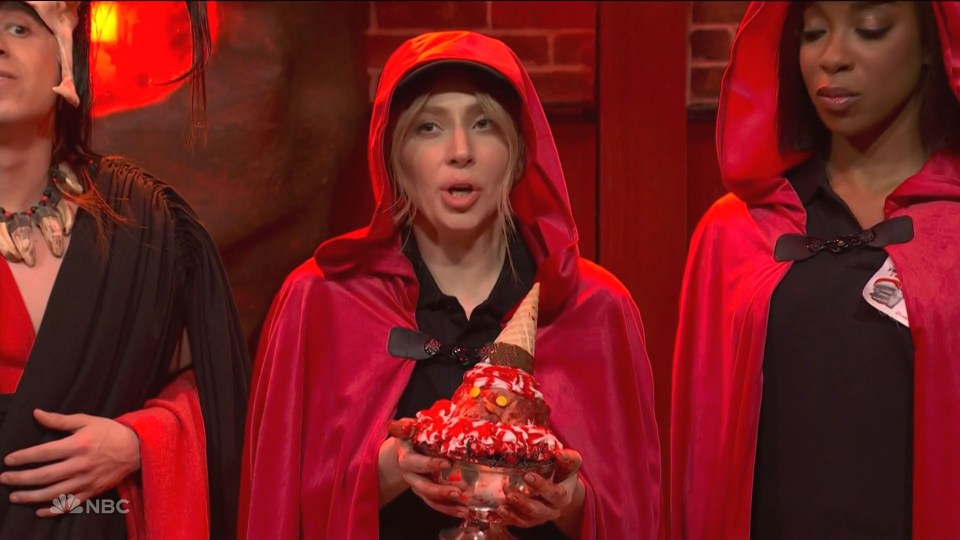 A woman in a red hooded cape holds a large ice cream sundae.