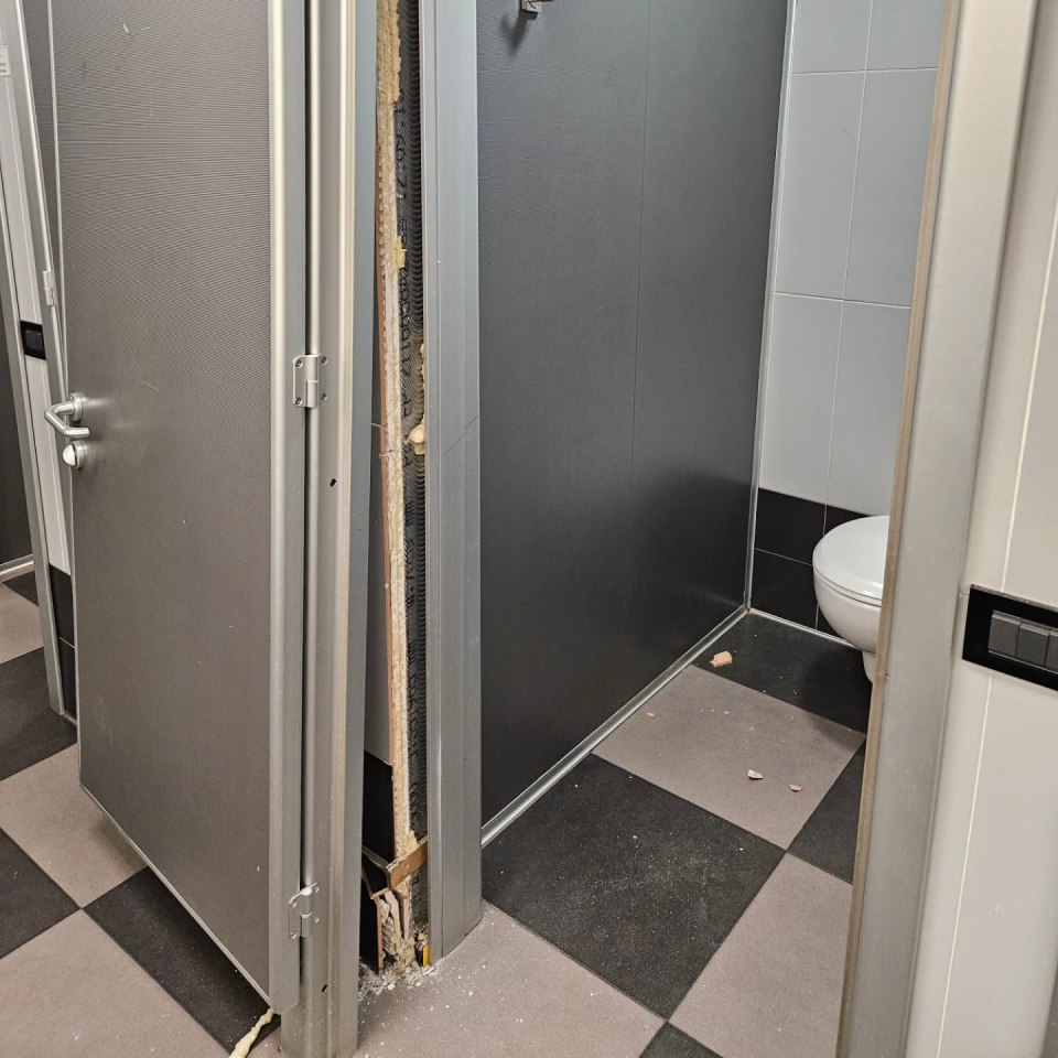 Damaged restroom stall door and wall.