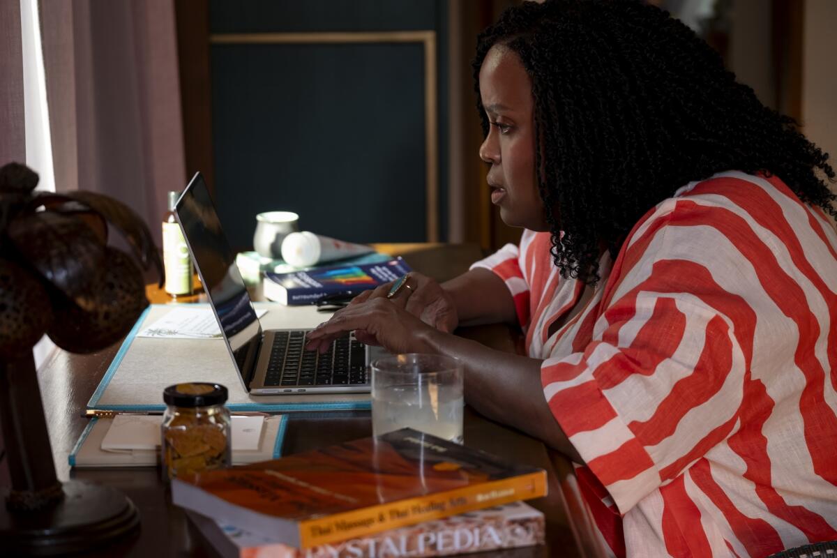 A woman in a red and white striped shirt looks intently at the screen of a laptop.