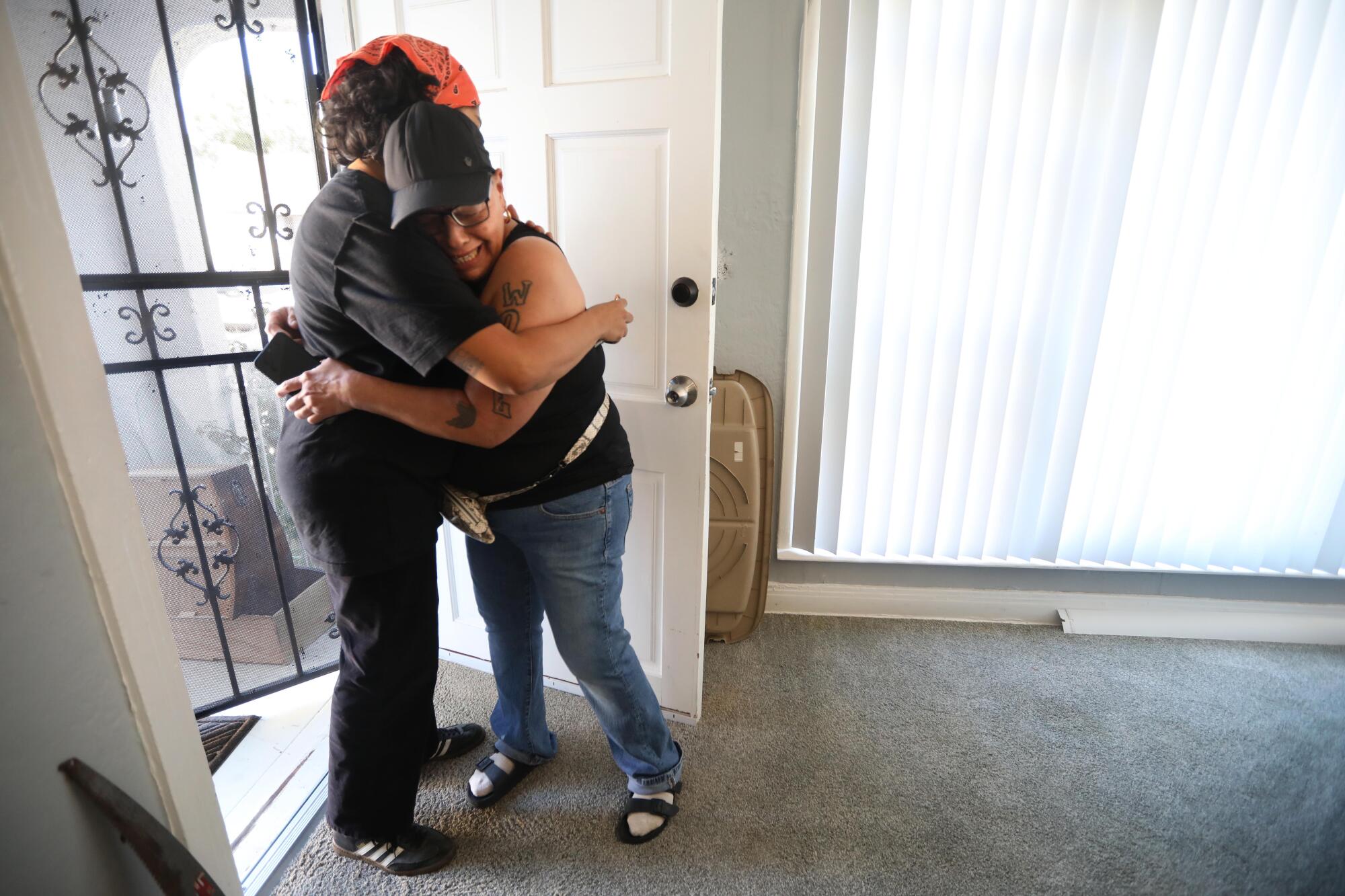 Two women, one of them crying, embrace at the door of a home.