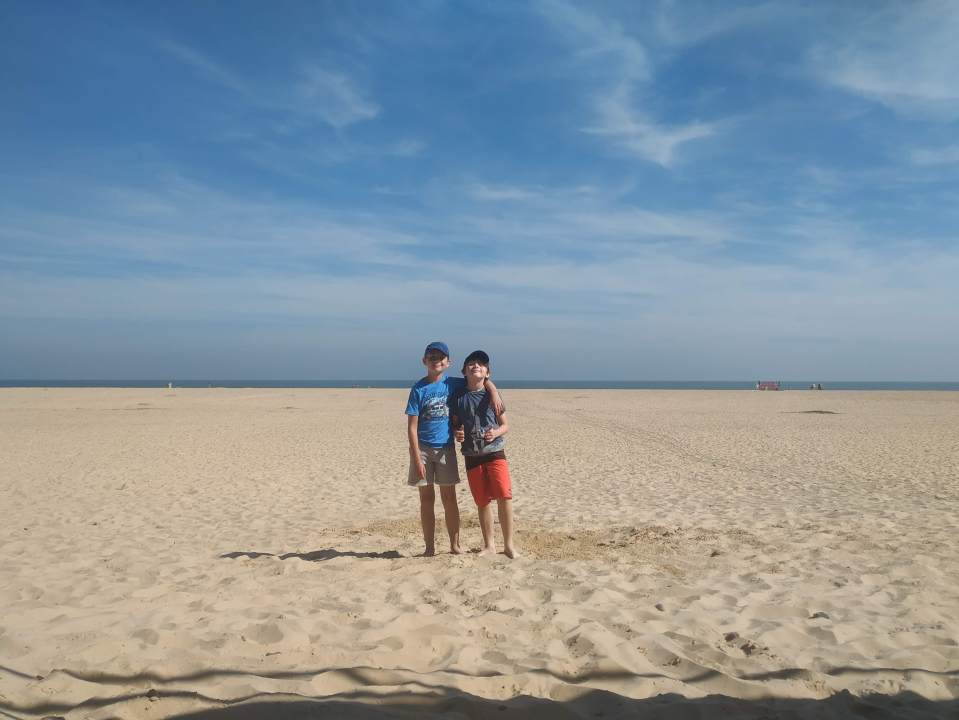 Two boys standing on a sandy beach.