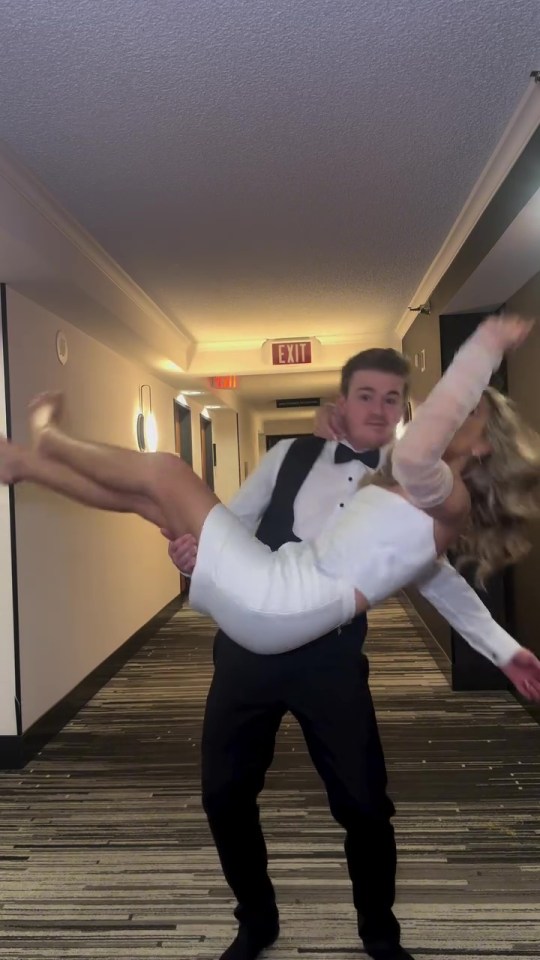 A man carrying a woman in a white dress down a hotel hallway.