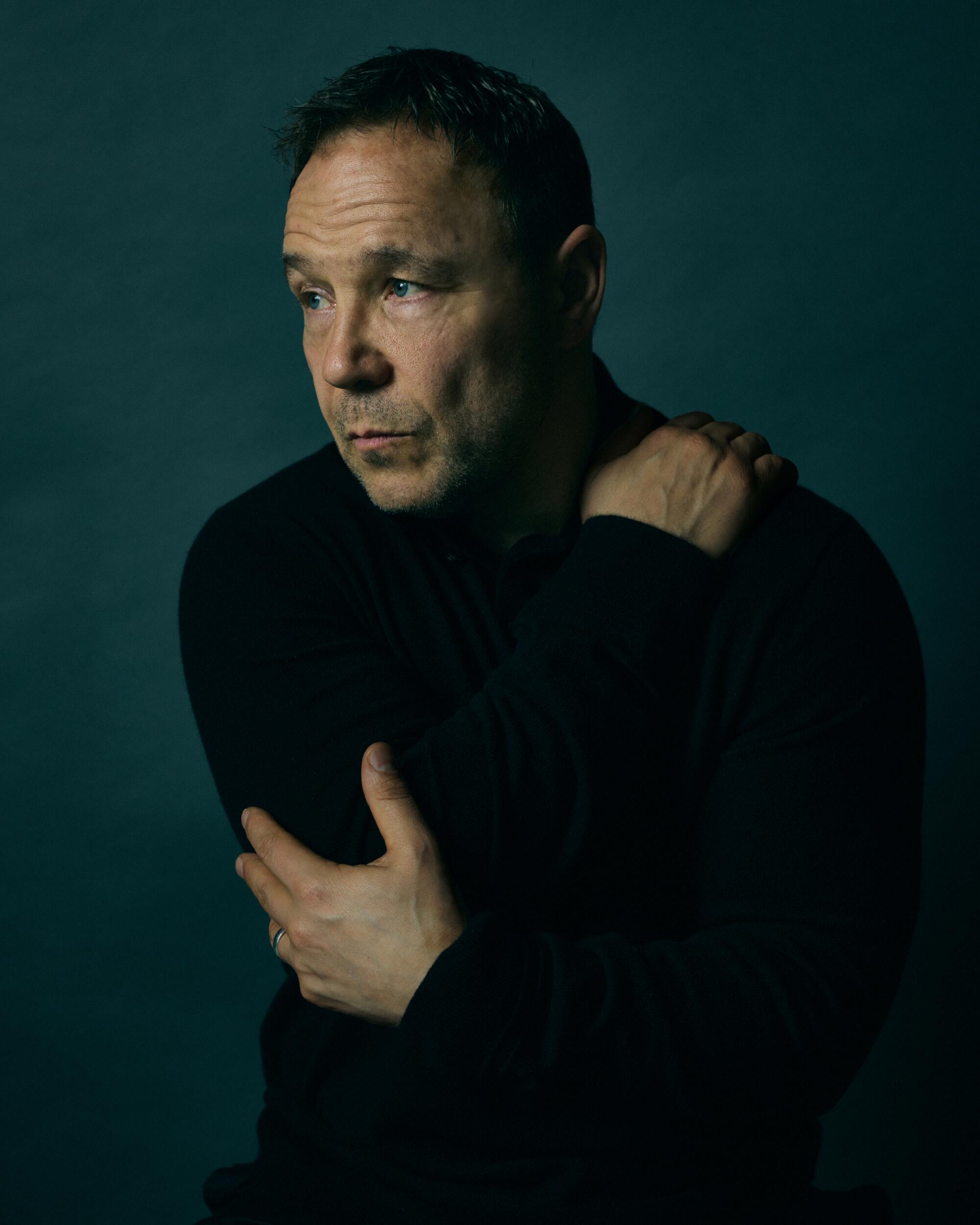 A man in a dark shirt with his arms wrapped around himself.