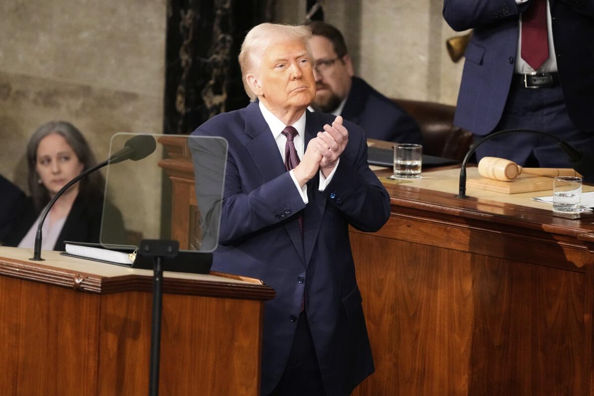 President Trump stands, clapping, behind a wooden lectern