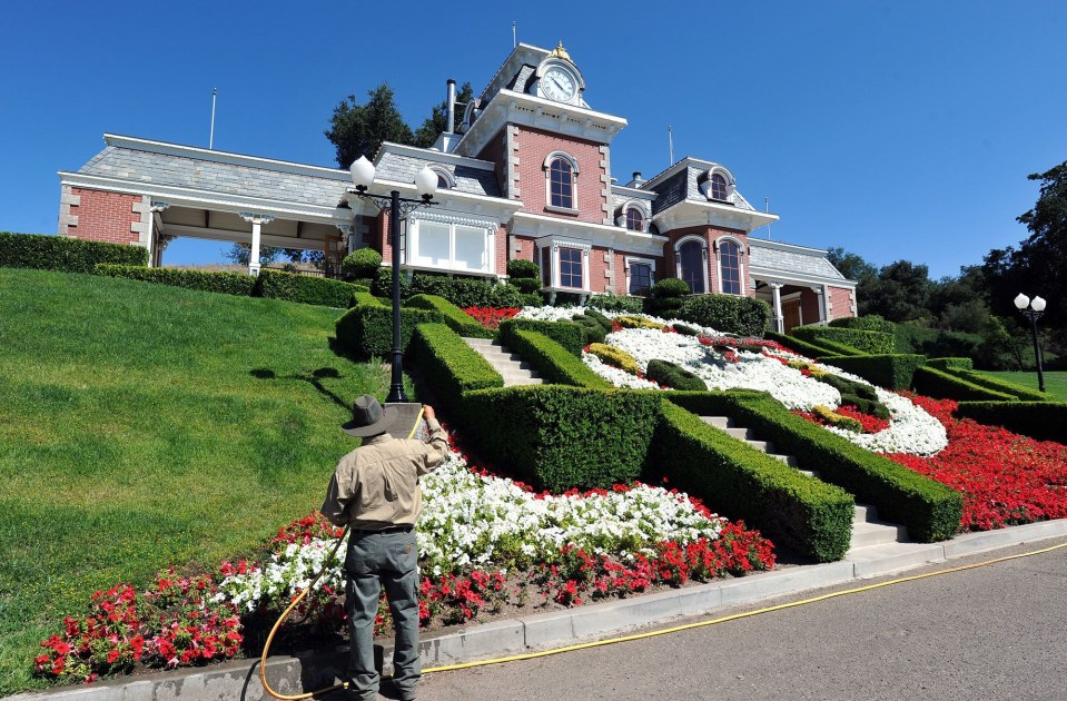 Groundskeeper watering flowers in front of a miniature Disneyland train station at Michael Jackson's Neverland Ranch.