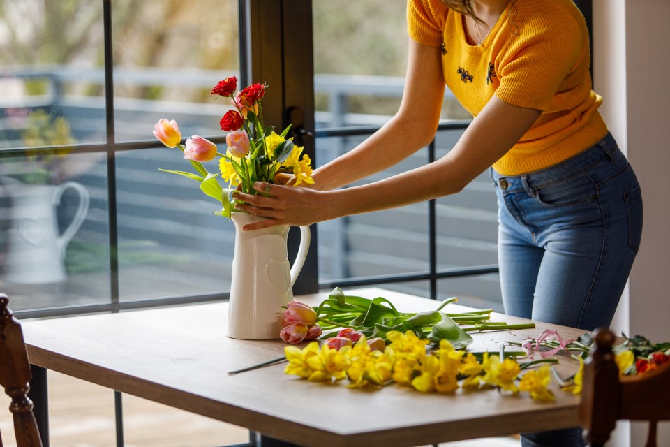 A young woman arranging tulips, daffodils, and roses in a vase.