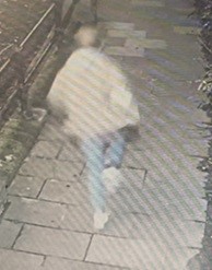 Blurry security camera image of a person walking away.