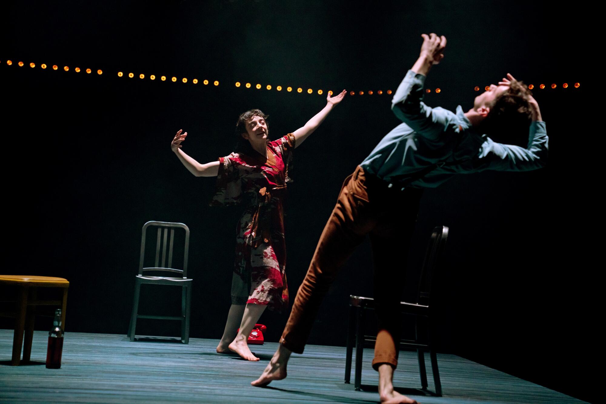 Two people dancing, arms upraised, on an impressionistic living room theater set with chairs