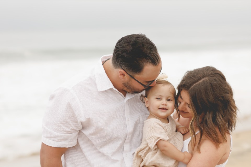 Family at the beach; a man and woman hold a baby.