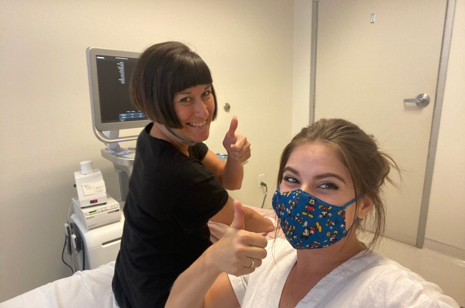 Two women giving thumbs up in a medical setting.