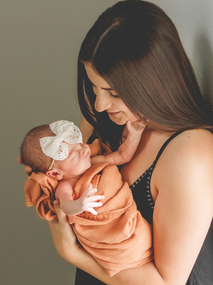 Woman holding a newborn baby wrapped in an orange blanket.