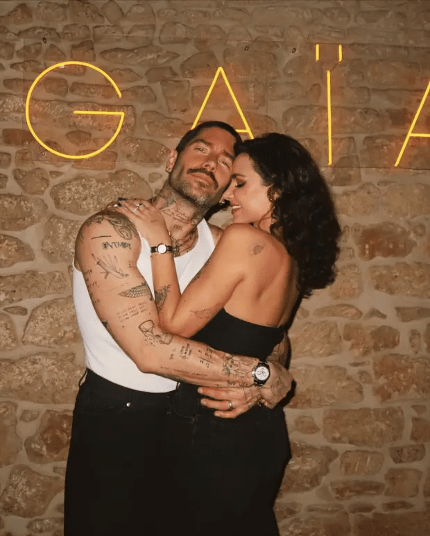 Couple embracing in front of a stone wall with a neon sign.