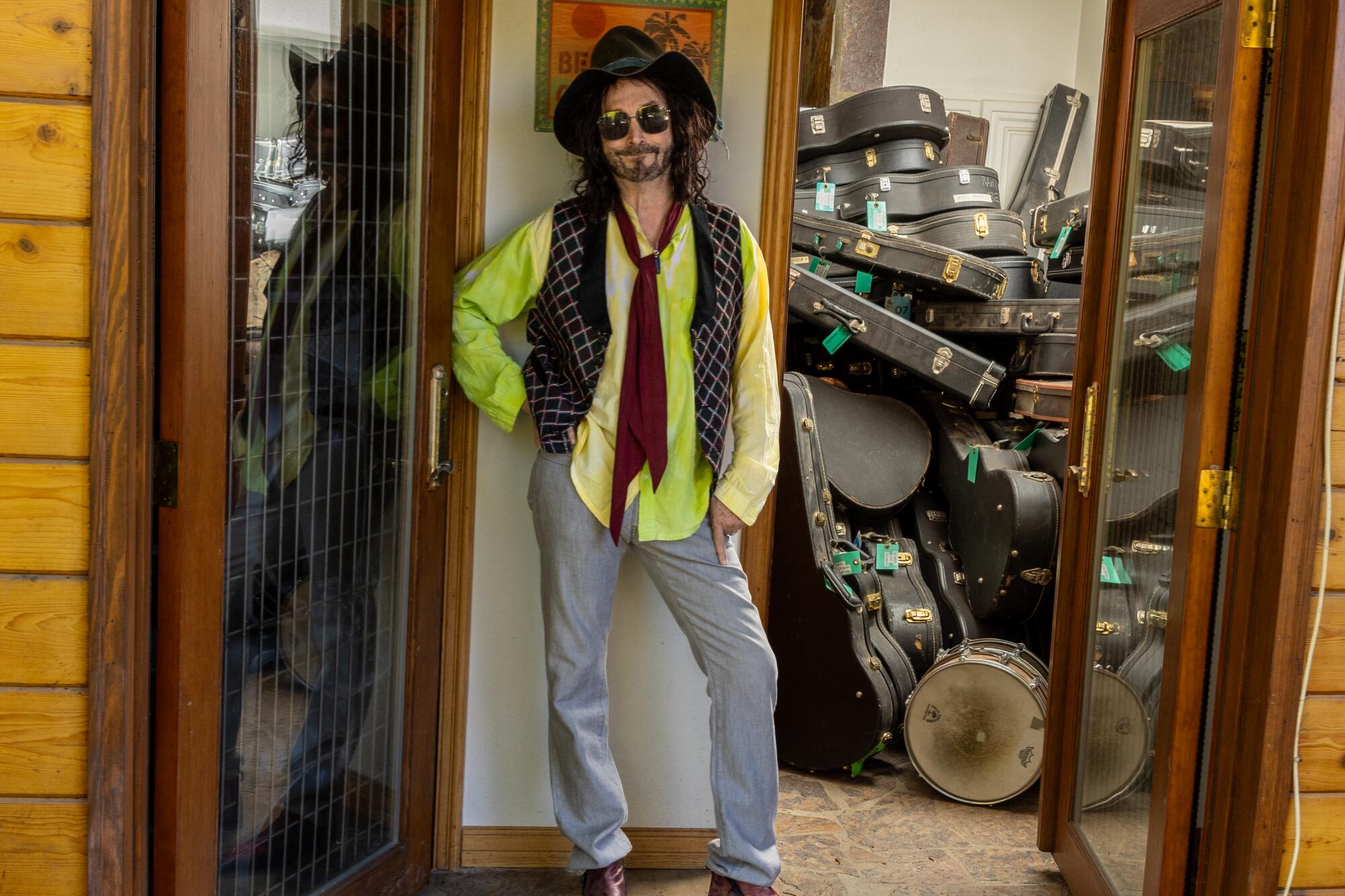 Mike Campbell stands in front of a room full of guitar cases.