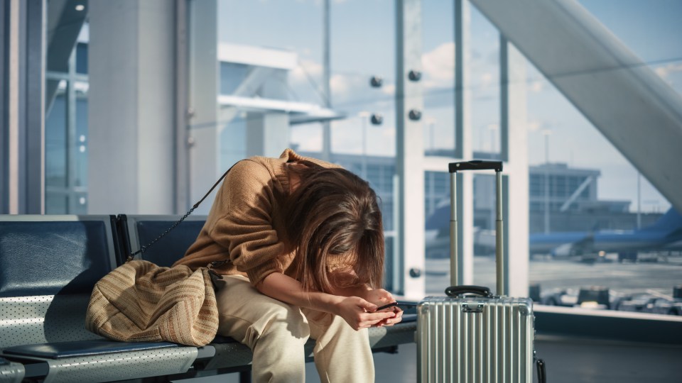 Woman sitting in an airport terminal, head down, looking at her phone.