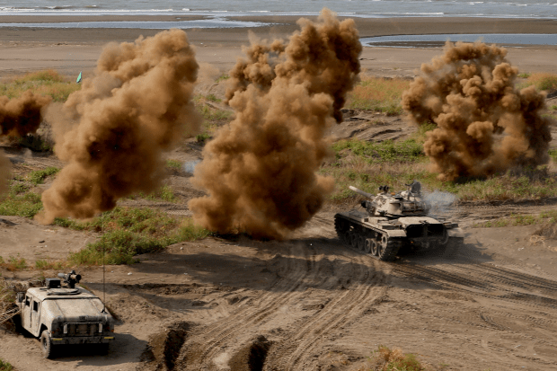 Military tank driving through explosions on a beach.