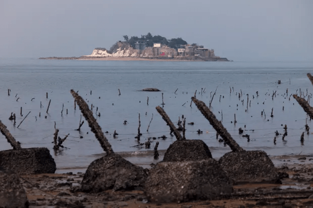 Coastal scene with weathered breakwater and island in the distance.