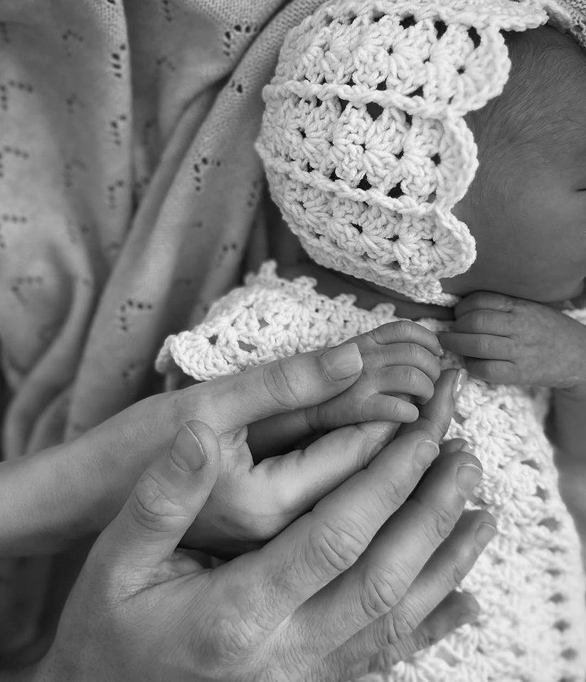 Black and white photo of adult hands holding a newborn's hand.