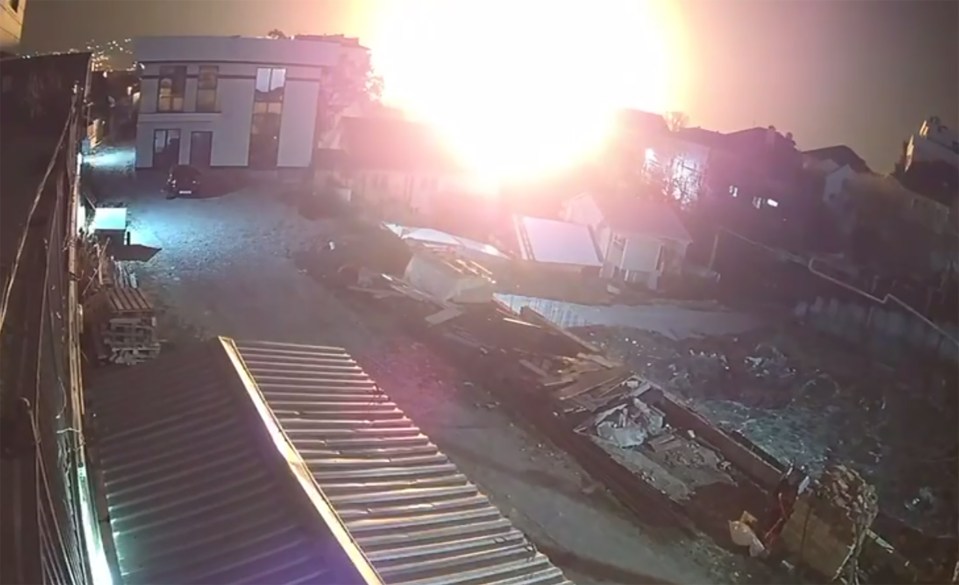 Nighttime security footage of a large explosion near residential buildings.