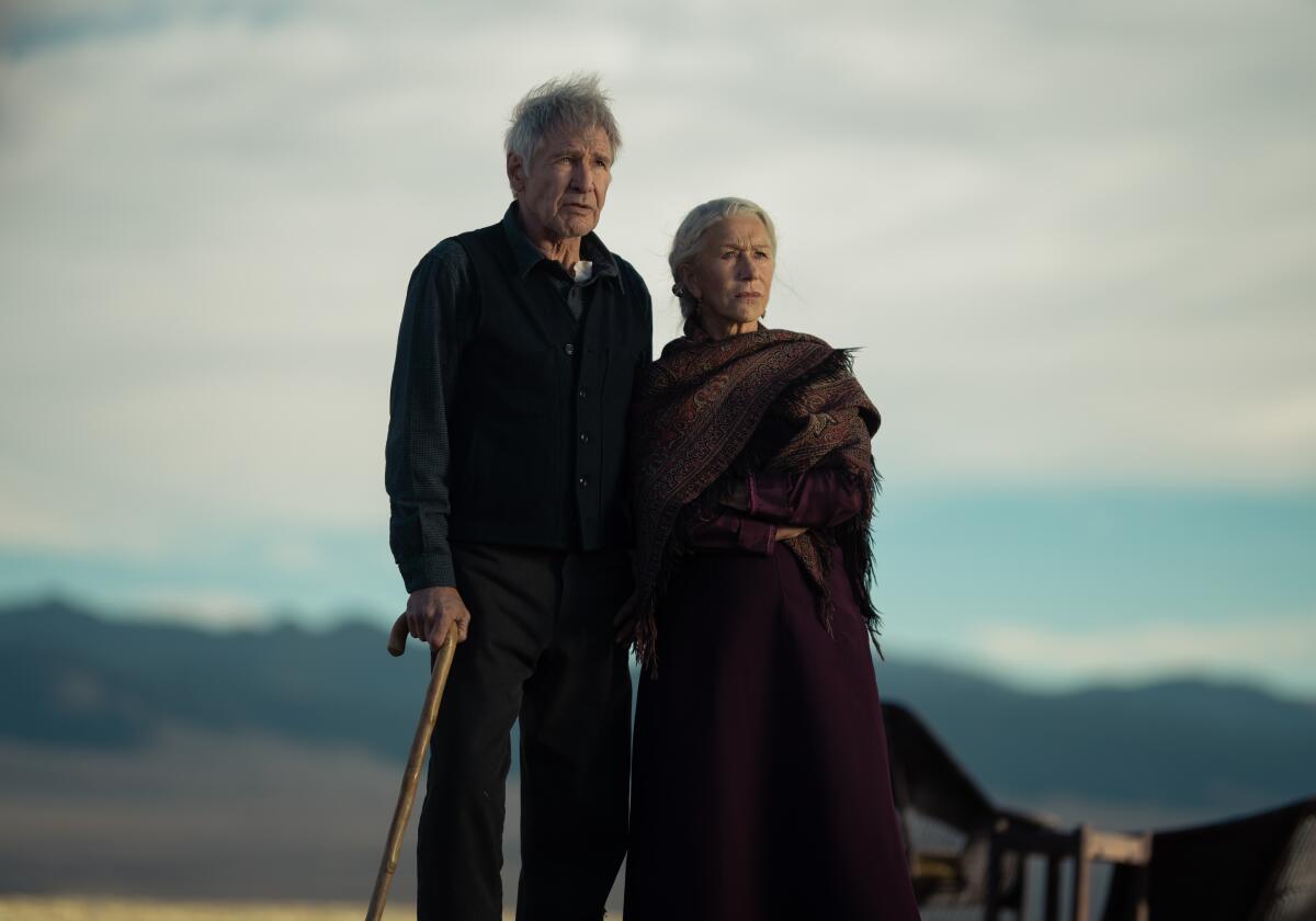 An older man holding a cane stands outdoors next to a woman as they stare out in the distance