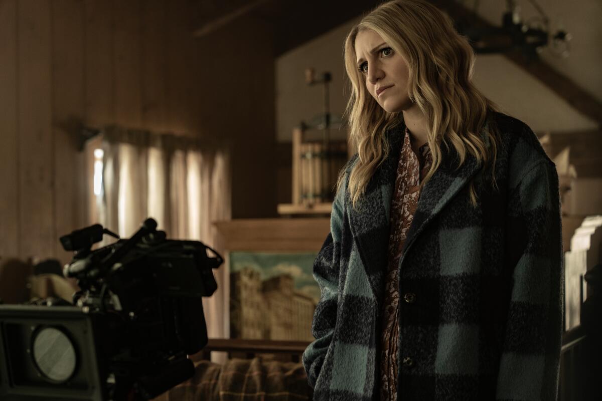 A blond woman stands next to a video camera that sits on a table