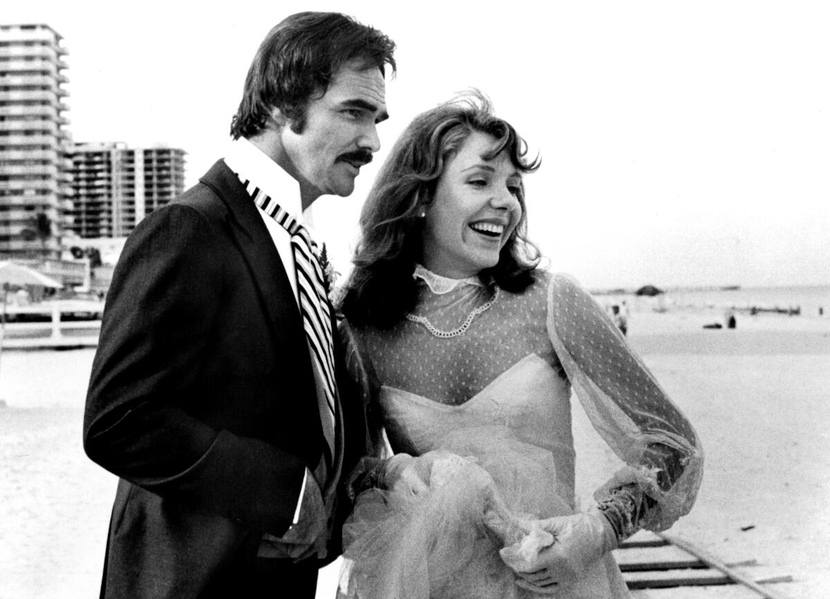 Two actors in wedding clothes pose on a set.