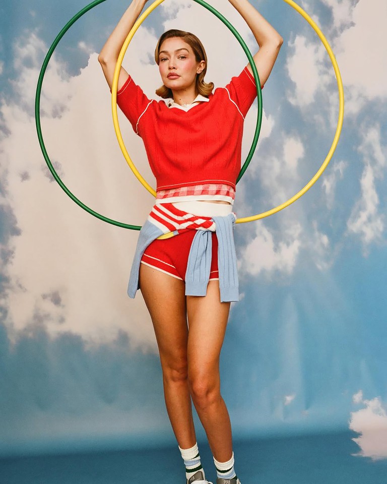 Gigi Hadid in red athletic wear, holding two hula hoops.