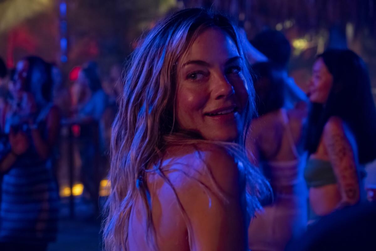 A woman with blonde wavy hair looks over her shoulder on the dancefloor of a club.