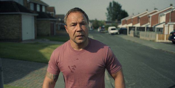 Stephen Graham in a red top on a street in a scene from Adolescence.