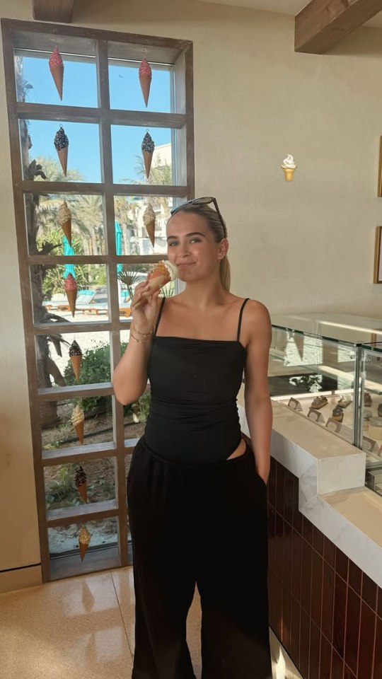 Woman eating ice cream cone in front of window with ice cream cone decorations.