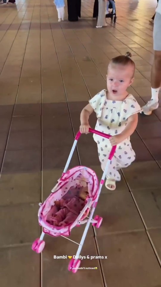 Toddler pushing a pink doll stroller.