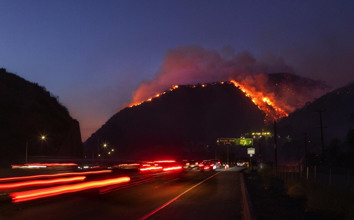 Traffic continues as flames roar up a steep hillside near the Getty Center in Los Angeles