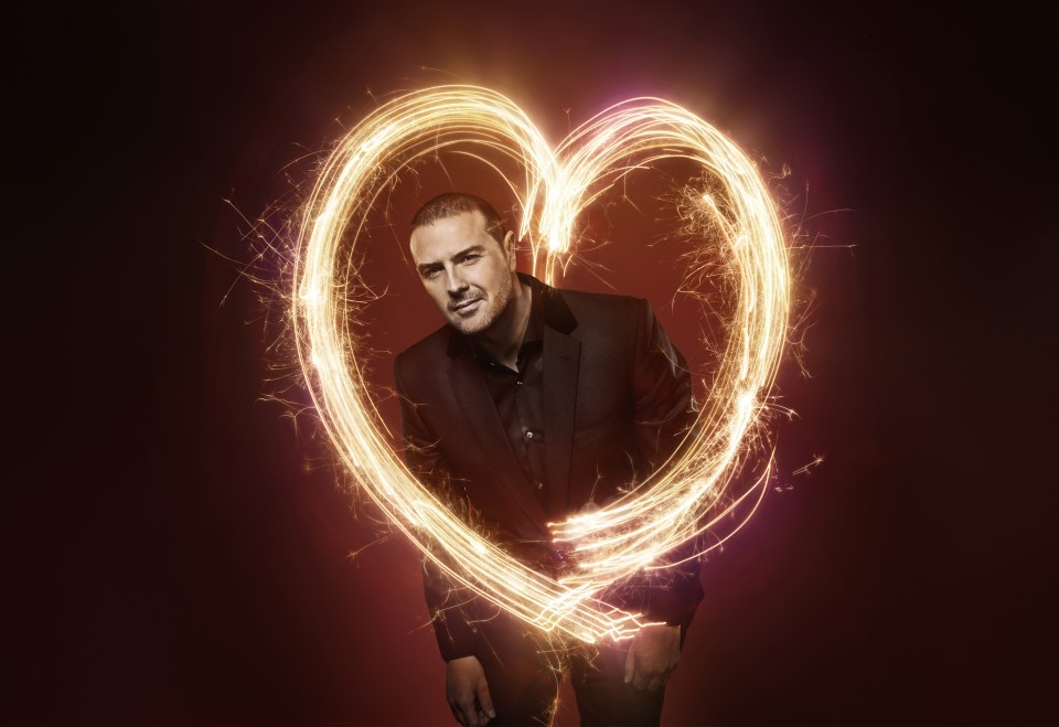 Man in a suit standing within a heart-shaped sparkler light trail.