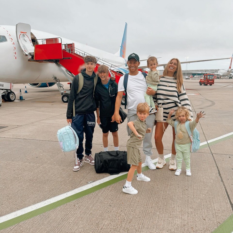 Family posing for a photo at the airport in front of a plane.